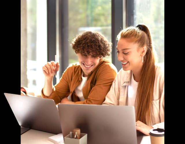 Dwoje uśmiechniętych młodych osób patrzy w ekran laptopa.