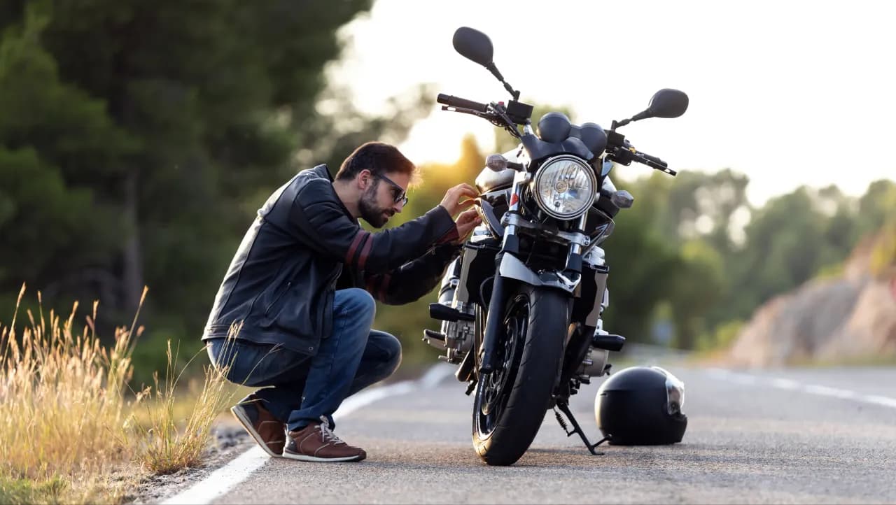 motocyklista sprawdza \coś w swoim motocyklu zaparkowanym na poboczu drogi